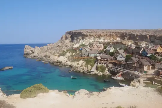 Malta co zwiedzić? Urokliwa wioska rybacka z kolorowymi domkami nad turkusową zatoką, wciśnięta między skaliste klify.