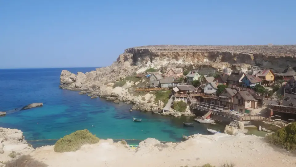 Malta co zwiedzić? Urokliwa wioska rybacka z kolorowymi domkami nad turkusową zatoką, wciśnięta między skaliste klify.